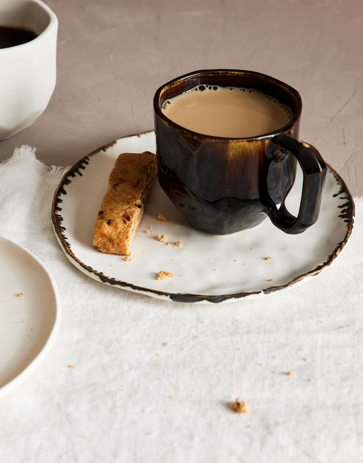 Handmade ceramic coffee mug with faceted shape and a glossy brown french roast glaze, filled with creamy coffee